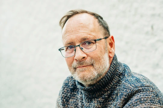 Portrait of a smiling mature man with glasses and a grey sweater, representing verified consumer satisfaction with mental clarity.