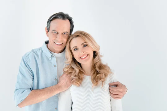 Happy adult couple smiling together against a bright white background, showcasing peak physical health and wellness.