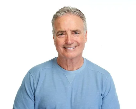 Portrait of a smiling mature adult man with grey hair in a light blue shirt, representing real consumer satisfaction.